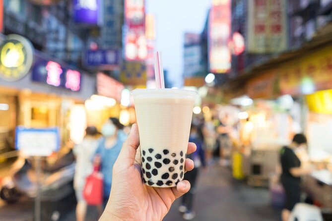 A cup of bubble tea held up in a lit Taipei night market street
