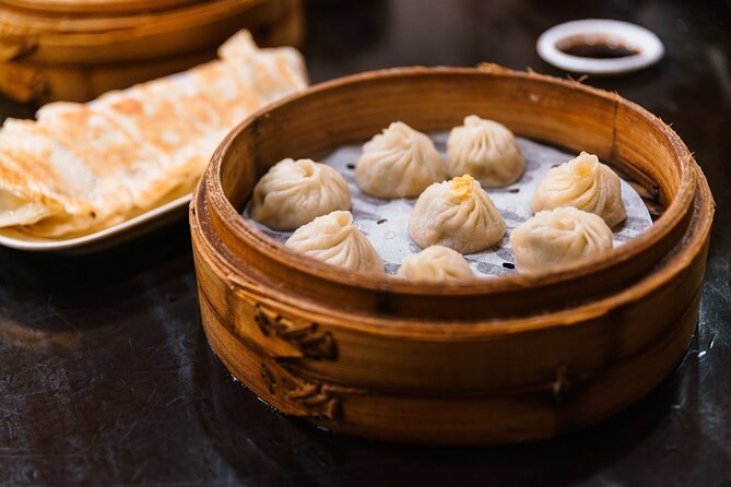 A bamboo steamer of xiaolongbao soup dumplings with a dish of vinegar